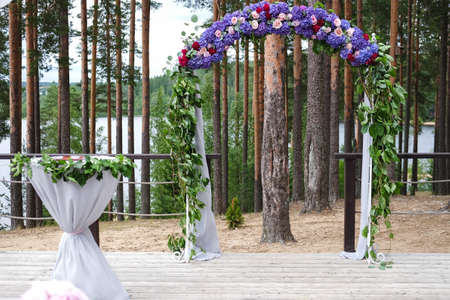 Wedding arch and grey chairs with peonies standing in ceremony area in woods.の写真素材