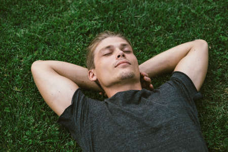 Attractive Young Man Lying with Both Hands Resting Behind his Neck on the Grassの写真素材