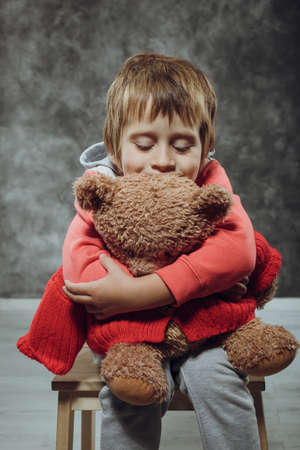 Boy 5 years old hugging big teddy bear sits on a chairの写真素材