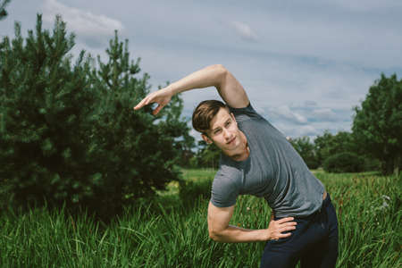 Male runner doing stretching exercise, preparing for morning workout in the parkの写真素材