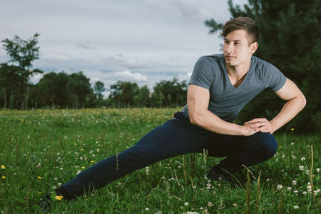 Male runner doing stretching exercise, preparing for morning workout in the park