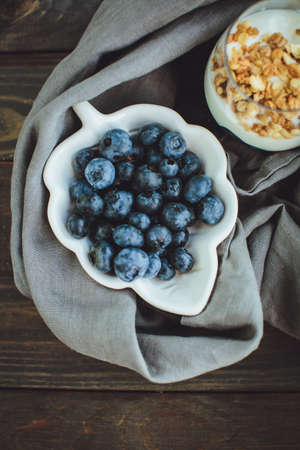 Yogurt with granola and fresh blueberries, in glass bowl over old wood background. Vintage effect.の写真素材