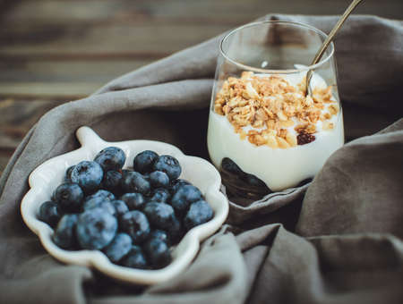 Yogurt with granola and fresh blueberries, in glass bowl over old wood background. Vintage effect.の写真素材