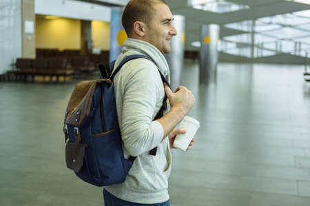 Passenger with Coffee Cup in Hand and Backpack  Sitting at the Hall of Airport Travel Conceptの写真素材