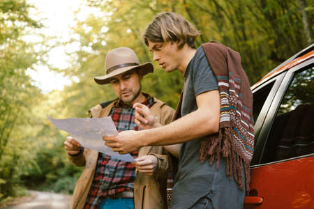 Traveler  man with hat  looking map near car in autumn forestの写真素材