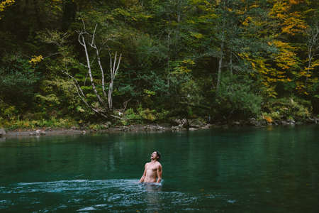 Young sports man bathing in a mountain lake in the fallの写真素材