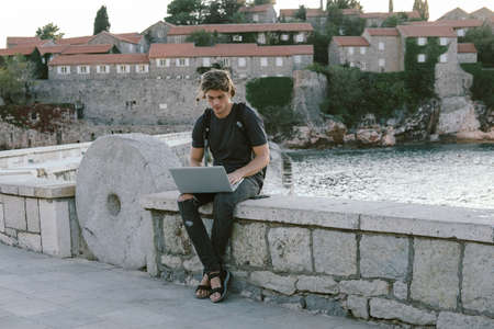 Charming Young man working on laptop near the sea, freelance working, social networks and online shopping conceptの写真素材