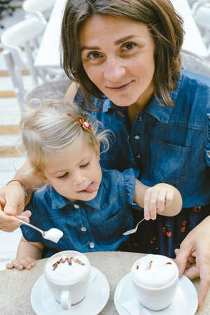 Happy mom and daughter eating drinking coffee outdoors.の写真素材