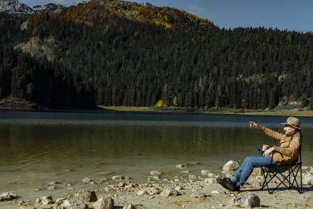 Handsome man in the hat is drinking coffee and enjoying the view of Black Lakeの写真素材