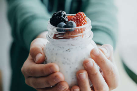 Closeup Boy hands with Pudding with chia seeds, yogurt and fresh fruits: Strawberries, blueberries...