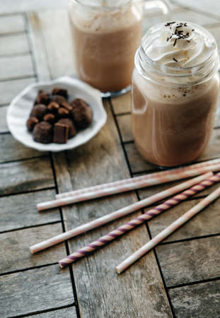 Iced chocolate with milk in retro glass jar (Mason Jar), pink straw and candy on wooden table.の写真素材