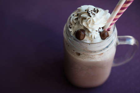 Homemade hot cocoa with whipped cream topping  in retro glass jar (Mason Jar), pink straw and candy on violet background.の写真素材