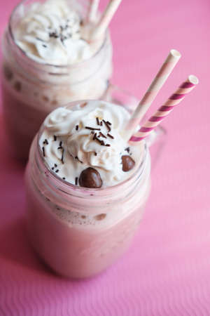 Homemade hot chocolate with whipped cream topping  in retro glass jar (Mason Jar), pink straw and candy on pink backgroundの写真素材