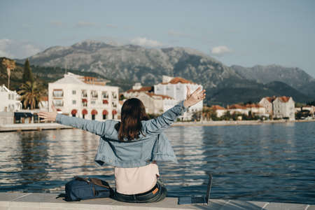 Back view of happy woman raised hands sitting on Embankment with laptop. Vacations, freelancer, lifestyleの写真素材
