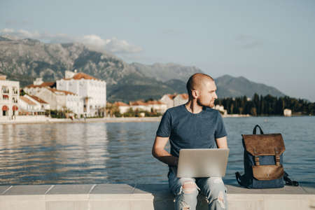 Young man sitting and working with laptop computer near the seaの写真素材