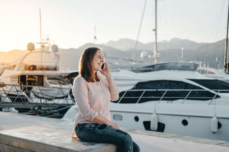 Portrait of smiling woman talking on the phone near Sailboats in harbour, seaside.の写真素材