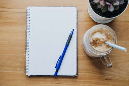 Notebook, pen, coffee, house plant on the table. Planning concept, flat lay, top view