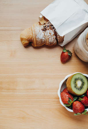 Top view of sweet breakfast with Coffee, croissant, strawberry, kiwi on a wooden tableの写真素材