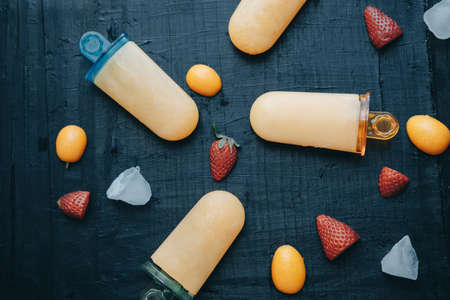 Homemade fruit ice cream with strawberries and kumquat on a black board.