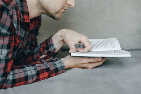 Handsome Hipster man in red checkered shirt reading book and lies on the couchの写真素材