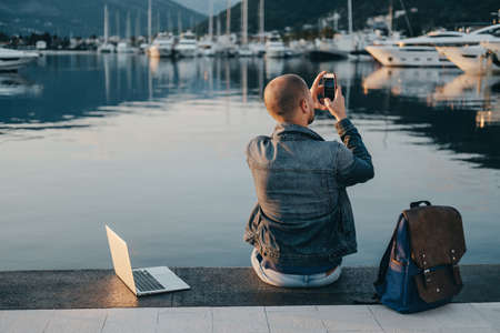 Young man freelancer working with laptop and taking photo  sitting near seaの写真素材