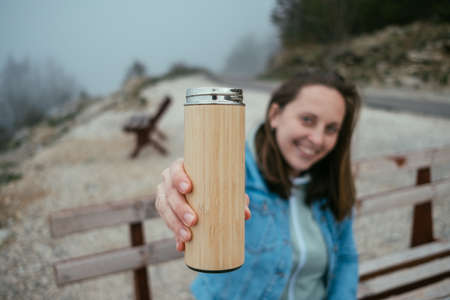 Closeup woman hand with thermos in autumn forest.の写真素材