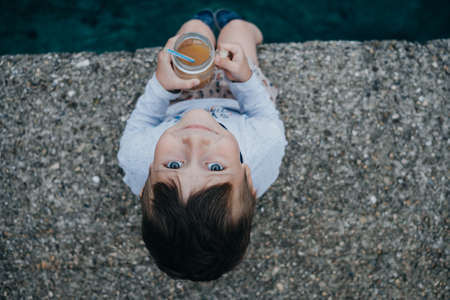 Little boy drinking juice At the pier by the seaの写真素材