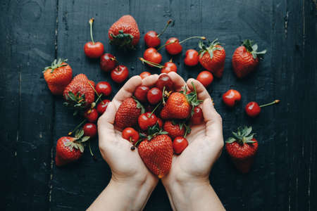 Woman hands with Fresh cherries and strawberries on the black wooden table, top viewの写真素材
