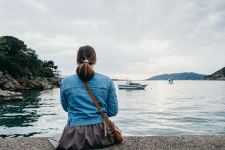 Back view of young  Woman is taking pictures of the sunset on the phone by the seaの写真素材