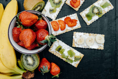 Delicious Crackers with cheese and fruits: bananas, strawberries and kiwi on a black background, Top viewの写真素材