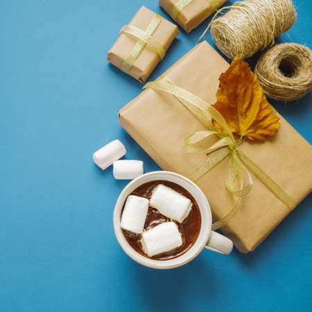 Hot chocolate with marshmallows and a gift on a blue background, flat lay, top view, space for textの写真素材