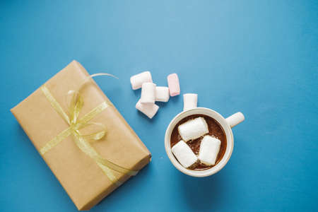 Hot cocoa with marshmallows and a gift on a blue background, flat lay, top view, space for textの写真素材
