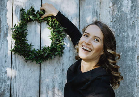 Portrait of smiling woman hanging a Christmas wreath on her homeの写真素材