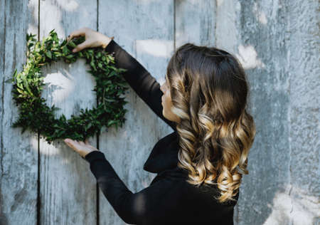 Preparing for Christmas. Young woman hanging wreath on her homeの写真素材