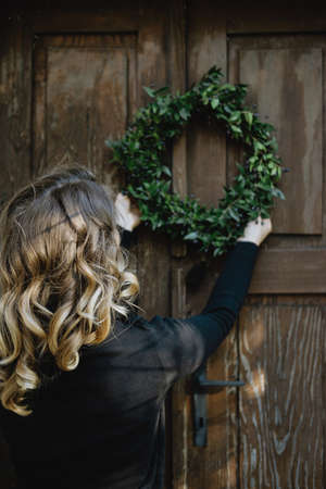 Back view of Young woman hanging a Christmas wreath on her homeの写真素材