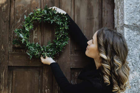 Young woman hanging a Christmas wreath on her homeの写真素材