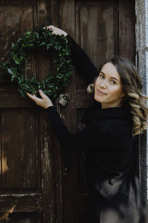 Portrait of smiling woman hanging a Christmas wreath on door of her homeの写真素材
