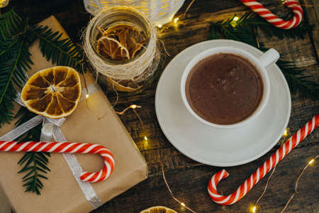 Closeup Hot chocolate with present, candy canes and Fir tree branch on dark wooden background....