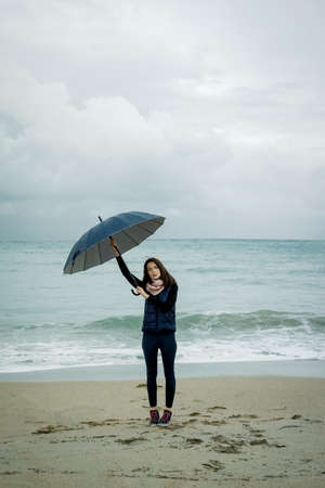 Young woman standing with an umbrella in front sea in winter or autumnの写真素材