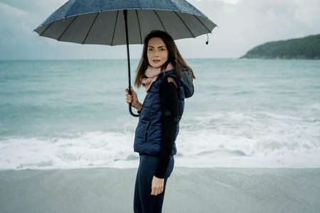 Young woman walking with an umbrella in front sea in winter or autumnの写真素材