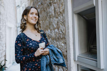 Woman traveler takes out money at an ATM in Europeの写真素材