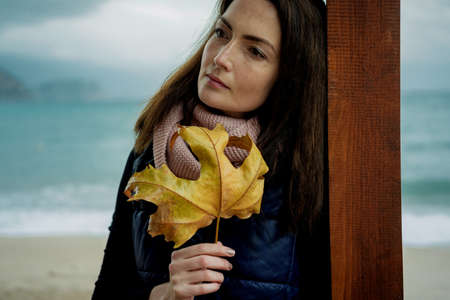 Beautiful Woman with Autumn Leaves against the sea in rainy dayの写真素材