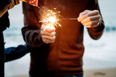 Closeup young beautiful happy couple holding sparkles against the sea. の写真素材