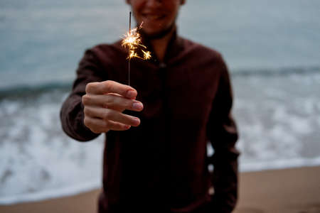 Happy smiling man holding sparkler near the seaの写真素材