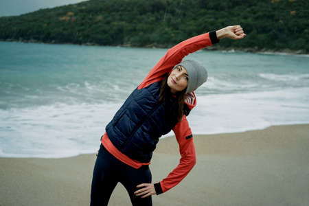 Young woman wearing a sports vest exercising by winter sea の写真素材