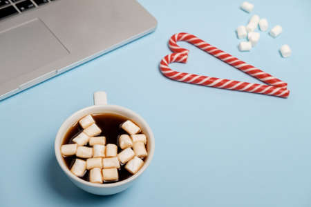 Closeup photo of Hot Cocoa with marshmallows and laptop, candies on a blue table. Christmas, flat layの写真素材