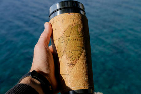 Closeup photo of thermal mug with tea in traveler's hand over sea view