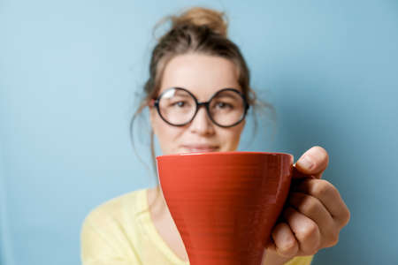 Closeup red mug in woman hands on a blue background. Studio shot