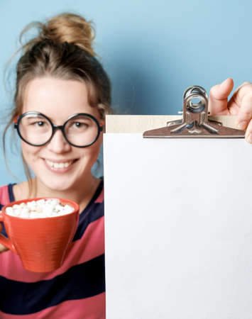 Beautiful young woman with with an empty sheet and  red mug on a blue background. New Year Resolutionsの写真素材
