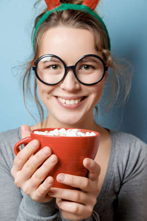 Beautiful young woman with a red mug on a blue background. Studio shotの写真素材